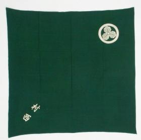 FUROSHIKI cloth, Japan, Showa (circa 1950), cm 105x103.  
Furoshiki were (and still are to some extent) wrapping cloths used when carrying small personal belongings, or to eventually wrap a gift to be presented. They have usually plain ground and display a large family crest (komon) in the centre as an identification tool.
This one, differently, shows a smaller pawlonia �komon� on a corner and some kanji character opposite to it, dyed using the tsutsugaki technique. The  rich, dark green colour has been achieved by over-dyeing indigo with a yellow dye. Good condition with just a few small stains.
