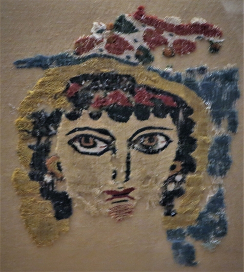 Fragment of Coptic woollen tapestry, probably a screen curtain, with the expressionistic head of a female figure, perhaps the personification of Spring. 3rd-4th c. 0.20x0.19 m. (ΓΕ 7177)Fragment of a linen tunic band, decorated with a grid pattern of lozenges and medallions with symmetrical motifs. From Egypt, 8th-9th c. 0.95x0.26 m. (ΓΕ 7173) Benaki Museum, Athens