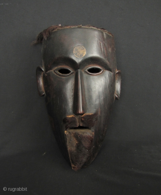 Nepalese Hill Tribe Mask:
Well carved tribal mask from Nepal. This is made from a heavy, densely grained wood with an old Nepalese rupee set in the forehead and an animal hide goatee  ...