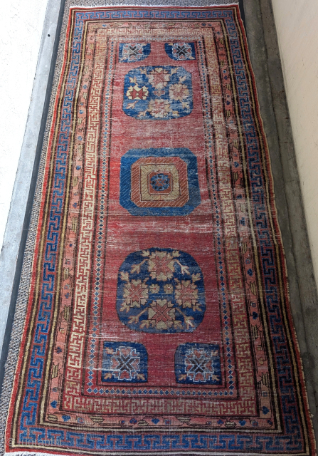 Rare unusual Khotan rug with a seldomly seen central medallion variant and corner pieces. Fret guard border is drawn very freely with little regularity. Worn, scattered repairs,both ends are rewoven.