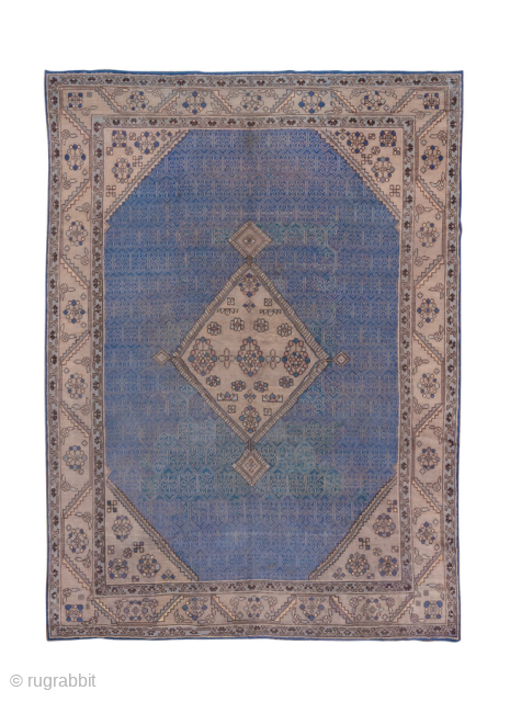 This antique Oushak rug features a rare and striking blue field with an elegant central medallion design. The geometric latticework across the field creates depth and texture, while the soft ivory border,  ...
