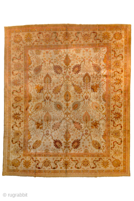 This antique Oushak rug radiates warmth with its golden, apricot, and soft terracotta tones woven into a flowing allover design of stylized palmettes, vines, and floral sprays. The broad border frames the  ...
