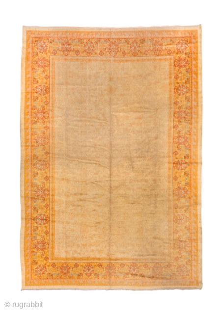 This antique Turkish Oushak rug, woven circa 1920, features a serene open field design in soft apricot and golden tones, framed by a delicately detailed floral border. Its large scale and harmonious  ...