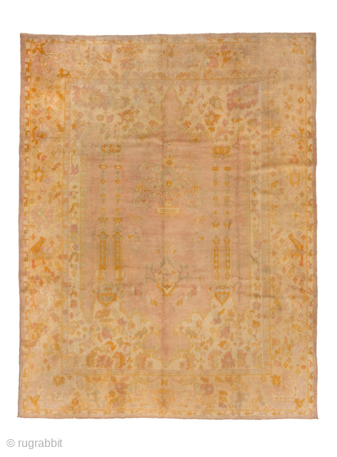 This antique Turkish Oushak rug, woven circa 1920, embodies the charm of Anatolian craftsmanship with its muted pastel palette of soft peach, gold, and ivory tones. The open field design is framed  ...