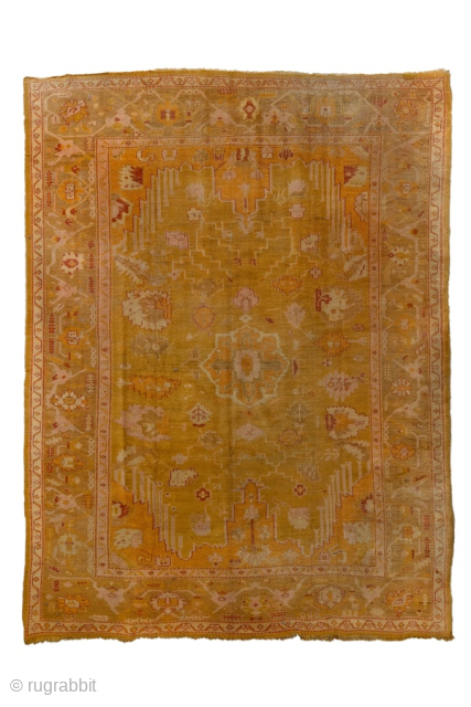 This antique Oushak rug glows with rich, warm tones of golden saffron, soft apricot, and muted blush. Its geometric medallion-and-corner design is framed by a beautifully drawn border, giving the rug a  ...