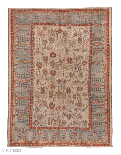 This antique Oushak rug, woven circa 1900, features a captivating Tree of Life design with stylized floral and botanical motifs cascading across an ivory field. The delicate, painterly pattern is framed by  ...