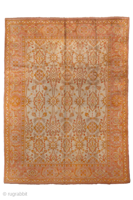 This antique Oushak rug, woven circa 1920, boasts a luminous palette of soft coral, apricot, and golden hues accented by subtle ivory highlights. Its allover pattern features stylized floral and geometric motifs  ...