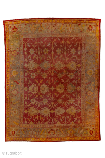 This antique Turkish Oushak rug, woven circa 1900, features a striking deep red field adorned with soft gold and muted blue floral motifs. The wide, decorative border frames the design beautifully, showcasing  ...