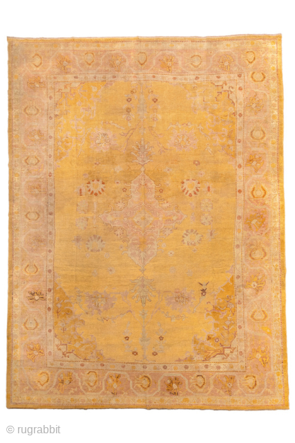 This antique Oushak rug features a luminous golden ground with soft rose undertones, creating a warm and inviting palette that is both refined and versatile. At the center, a faintly drawn medallion  ...