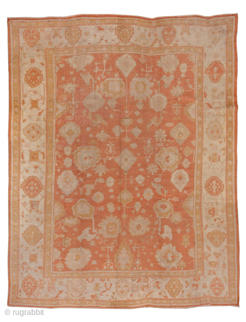 This grand antique Oushak rug from Western Anatolia features a luminous terracotta field adorned with large-scale floral and palmette motifs in soft ivory, pale gold, and muted beige. The expansive design, combined  ...