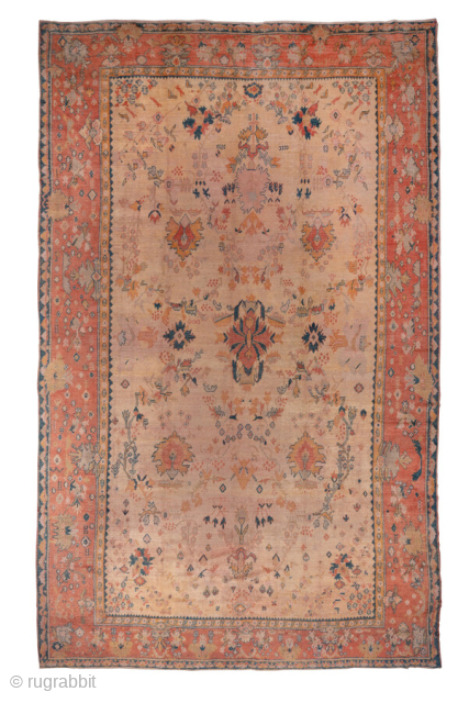 This magnificent large-scale antique Oushak rug features a serene and graceful composition typical of early 20th-century Western Turkish weaving. The soft coral field hosts a loosely drawn floral medallion pattern rendered in  ...