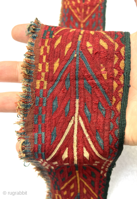 “An early 19th-century Tekke Turkmen embroidered band, featuring intricate abstract motifs in shades of red, blue, yellow, white, dark green, and apricot yellow. This embroidery is entirely silk, stitched onto a red-brown  ...