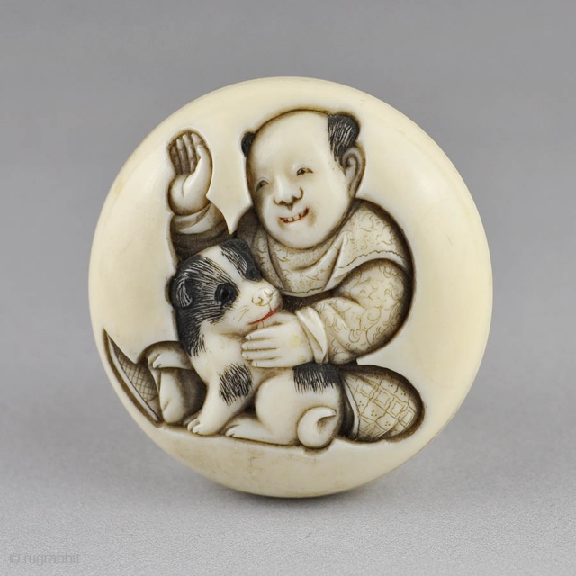 Japanese ivory manju netsuke carved in low relief  with a boy and puppy, 
the reverse is carved with another puppy end the carver's signature.
The details stained in black and red ink.
  ...