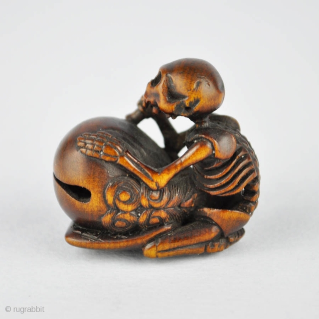 Japanese wood netsuke finely carved with the skeleton of the priest Danka beating the mokugyo, 
the wooden bell used in the Buddhist liturgy. The himotoshi ringed in horn. Signed: Juzan 寿山
19th century.  ...