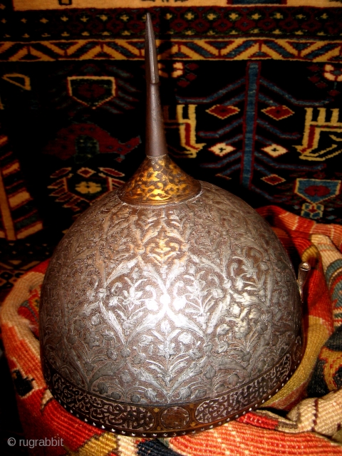 A fine Persian Safavid helmet c 1700. Heavy silver inlay with an engraved lattice pattern and floral sprays in a style seen in some "Vase" carpets. There is gold plating around the  ...