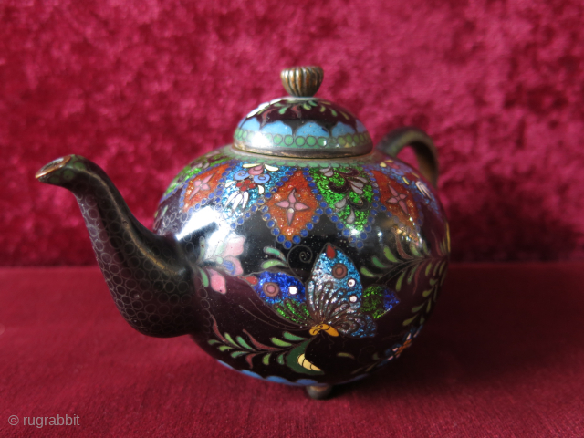 Antique Meiji era Japanese Cloisonne footed teapot. The teapot’s body is decorated all over with scrolling foliage and multicolored butterflies, flowers on a black background while the spout and the base are  ...