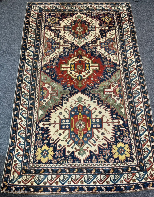 This 19th-century Caucasian Zeywa rug features a powerful geometric composition set against a deep midnight blue field. The central axis is defined by three monumental "sunburst" medallions, complemented by four halved medallions ...