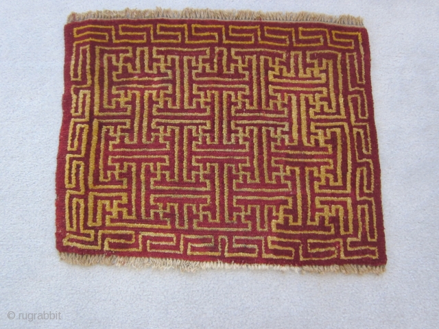 Tibetan mat, 19 by 24 inches, overall running swastika design in red and yellow, small repairs in field, upper 2 inches of border rewoven, early 20th C.      