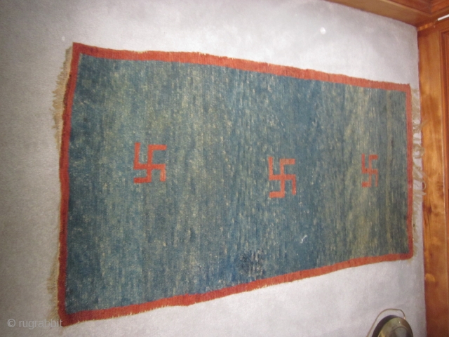 Tibetan khaden, pre-1900, 2'5" by 4'6", three eccentric swastikas on an abrashed blue ground, some quality repiling in field              