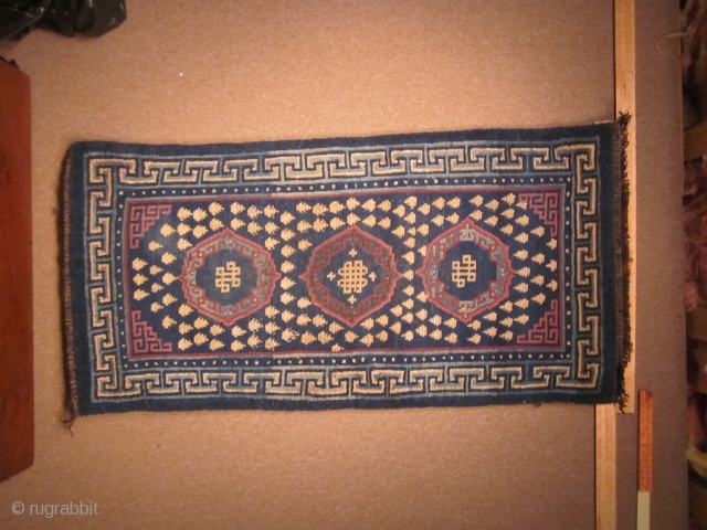Tibetan khaden, with traditional 3 coin (?gul) design and endless knots, in blue, off white and purple,c.1900, 29 by 71 inches, some reweaving at ends.        
