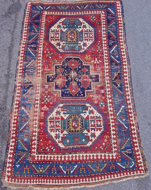 Colorful Kazak on a red ground with three medallions and several curious figures in the field.  3rd quarter of the 19th century. Size = 4'7" x 8'3". Inv. # 14692.  