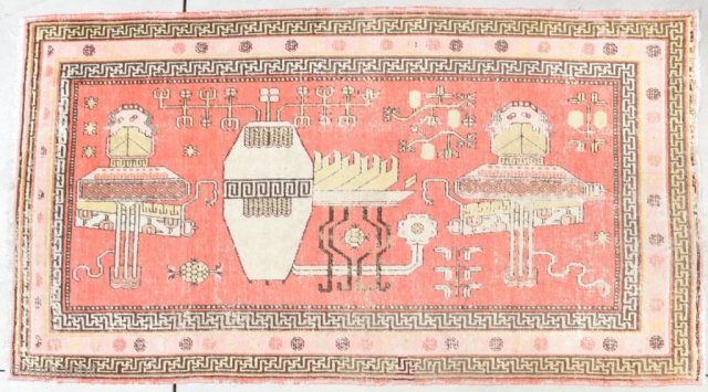 This circa 1920 Khotan Oriental Rug measures 5’5” X 9’9”. It has a center motif of a flower filled urn next to a table holding stylized images of something indescribable to me,  ...