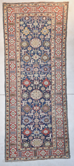 This pre 1850 Kuba measures 3’7” X 9’4”. It has a dark blue ground with a very interesting motif. There are 22 blossoms in shades of green, red, blue, and tobacco completely  ...