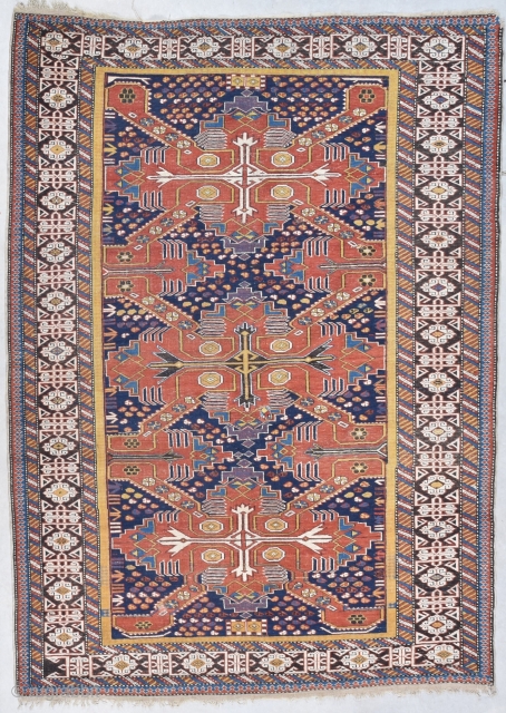 This circa 1880 Shirvan/Kuba measures 4’7” X 6’4”. It has three tomato red Saint Andrews crosses on an indigo ground. The ground is covered in quartered octagons in ivory, tobacco, two shades  ...