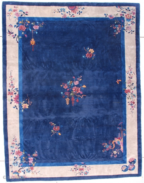 This circa 1920 Art Deco Chinese Oriental Rug measures 9’0” X 11’9” (274 x 362 cm). It has a navy blue field containing a floral motif consisting of a rockery coming from  ...