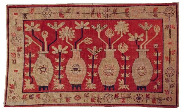 This circa 1920 Khotan #6203 
antique carpet measures 4’11” x 8’1”. It has four standing urns in pink and green on a red ground with flowers sprouting from each. It has a  ...