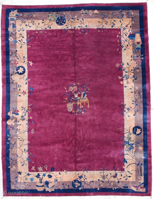 This circa 1920 Art deco Chinese rug measures 8’10’ x 11’7”. It has an urn of flowers with two tables with urns of flowers in the center of a raspberry open field,  ...