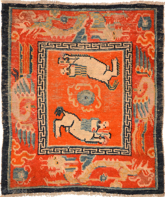 Tibetan over-saddle carpet (masho) featuring two playful-looking snow lions chasing a central flaming jewel in an orange center field. The outer border consist of dragons and phoenixes on somewhat more redish background  ...