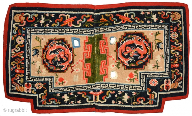 Tibetan under-saddle carpet or makden.  A single frolicking dragon is enclosed inside a mandala shaped outline on either side with flowers lightly scattered in the main field. The main outer border  ...