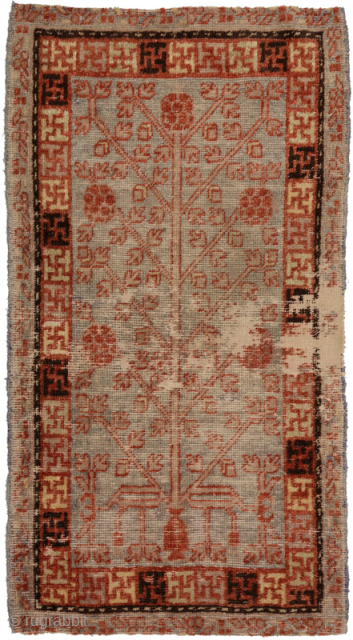 Well worn carpet from Chinese East Turkestan which appears to have been used as over-saddle carpet (or ‘masho’ in Tibetan). It features an asymmetric designed pomegranate tree-of-life sprouting out of a singular ...