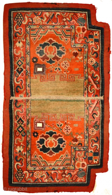 This Tibetan under-saddle carpet or ‘makden’ has a floral design on either side in a reddish-orange main field with abstract clouds and mountains at either end and is enclosed by a narrow,  ...