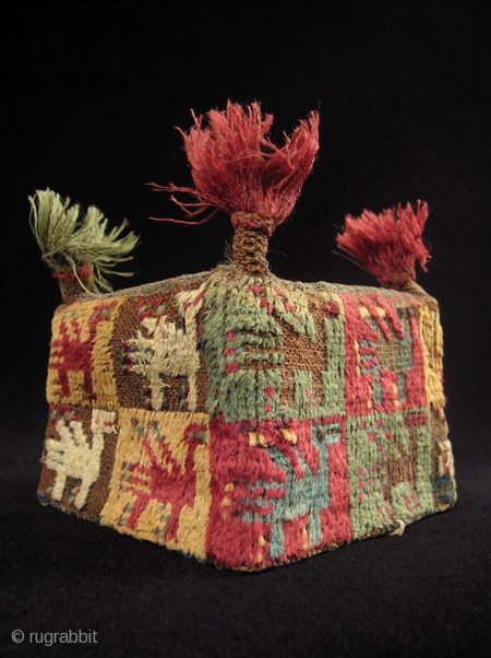 A colorful four-cornered hat from the Huari culture of the Highlands of Peru. Made of camelid wool yarns and natural dyes, it has a mesh screen on the top to contain the  ...