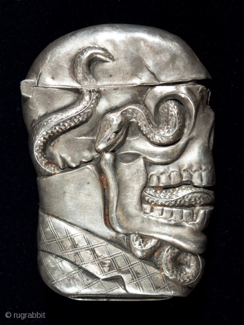 Match safe,
Unknown manufacturer.
Sterling silver.
2.5" (6.3 cm) high.
c. 1895.
This rare match safe is marked STERLING and there is a pinched striker on the bottom. A serpent winds through a dapper skull's sye sockets,  ...