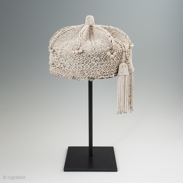 Beaded crown, Yoruba People, Nigeria. 8″ (20.3 cm) high by 7″ (17.8 cm) wide. Mid-20th century. A nice example with two tassels hanging on one side, some slight bead loss and a  ...