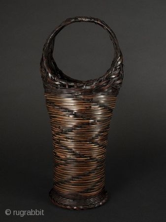 Japanese Antique Bamboo Basket

Japanese antique bamboo basket, tall narrow shape with circular handle. Design on body of zigzag alternating dark woven bamboo on lighter woven material. Ending in circular flattened foot. Interior  ...
