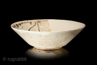 Fragment of a bowl, of conical form with steep flaring walls, stepped down to a low foot, slip-painted, decorated in brown on a slip ground with a single band of Kufic script  ...