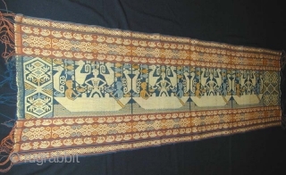 East Sumba Ceremonial Sash. Woven in supplementary-warp technique. Yellow and blue details are painted in after the weaving is completed. 199x57 cm. Mid-20th Century. Background colours are natural indigo and brown derived  ...