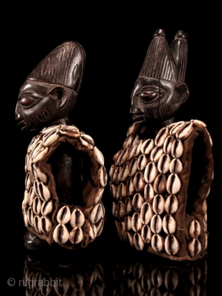 Ibeji, Yoruba sacred twins. Nigeria. Two wooden statues, each 25 cm ca high. Datable 2nd to 3rd q 20th century. Male & female. Both covered in a rich vest with over 130  ...