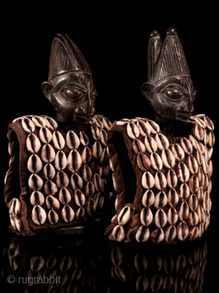 Ibeji, Yoruba sacred twins. Nigeria. Two wooden statues, each 25 cm ca high. Datable 2nd to 3rd q 20th century. Male & female. Both covered in a rich vest with over 130  ...