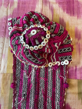 Tajik young girl's cap with the traditional "tail" to hide the plait. The cap is heavily embroidered in stripes of cherry red, alternating with white geometric bands, which show the dark ground.  ...