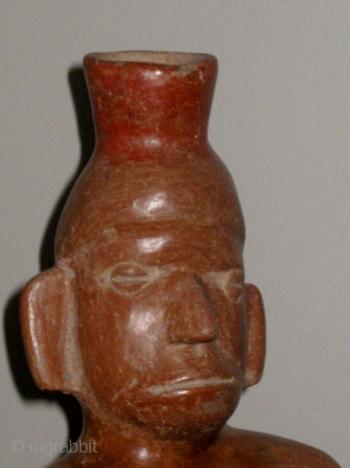 Pre-Columbian Colima figural vessel in the form of a seated male figure; 300BC to 300AD;  10 1/4" high.  Burnished reddish brown terracotta, with a dark fire bloom behind the right  ...