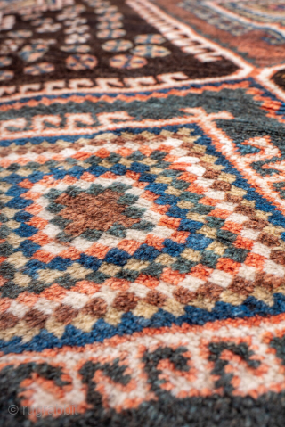 Antique Persian Kurdish Rug, circa 1910. Featuring bold diamond medallions on a dark field with scattered rosettes and tribal motifs, framed by a cream geometric border. Strong village character with lively, graphic ...