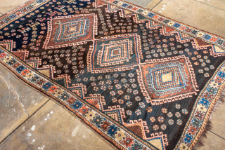 Antique Persian Kurdish Rug, circa 1910. Featuring bold diamond medallions on a dark field with scattered rosettes and tribal motifs, framed by a cream geometric border. Strong village character with lively, graphic ...