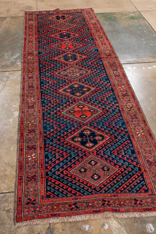 Antique Persian Kurdish Rug Runner, Circa 1900. Striking sequence of stepped diamond medallions connected by bold zigzag motifs woven across a rich midnight blue field framed by geometric tribal borders.
3'0" x 8'9"
Item ...