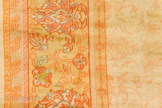 This antique Turkish Oushak rug, woven circa 1920, features a serene open field design in soft apricot and golden tones, framed by a delicately detailed floral border. Its large scale and harmonious  ...