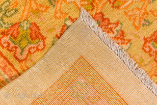 This antique Turkish Oushak rug, woven circa 1920, features a serene open field design in soft apricot and golden tones, framed by a delicately detailed floral border. Its large scale and harmonious  ...
